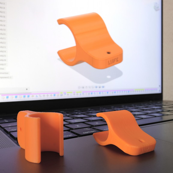 Orange 3D printed clips on a laptop computer, showing the CAD drawing of the clips