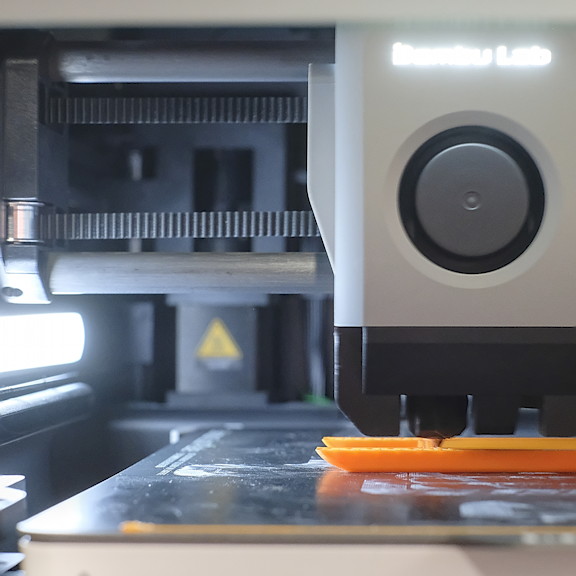 Close up of a 3D printer printing an orange object